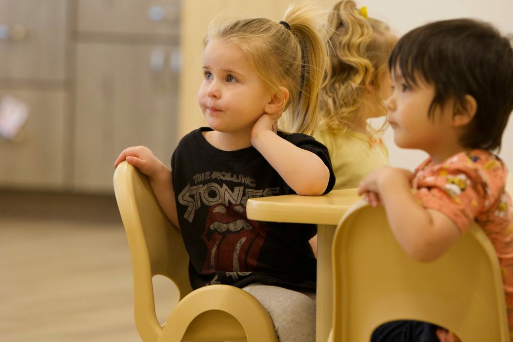 Toddlers seated at small chairs in a home-style room